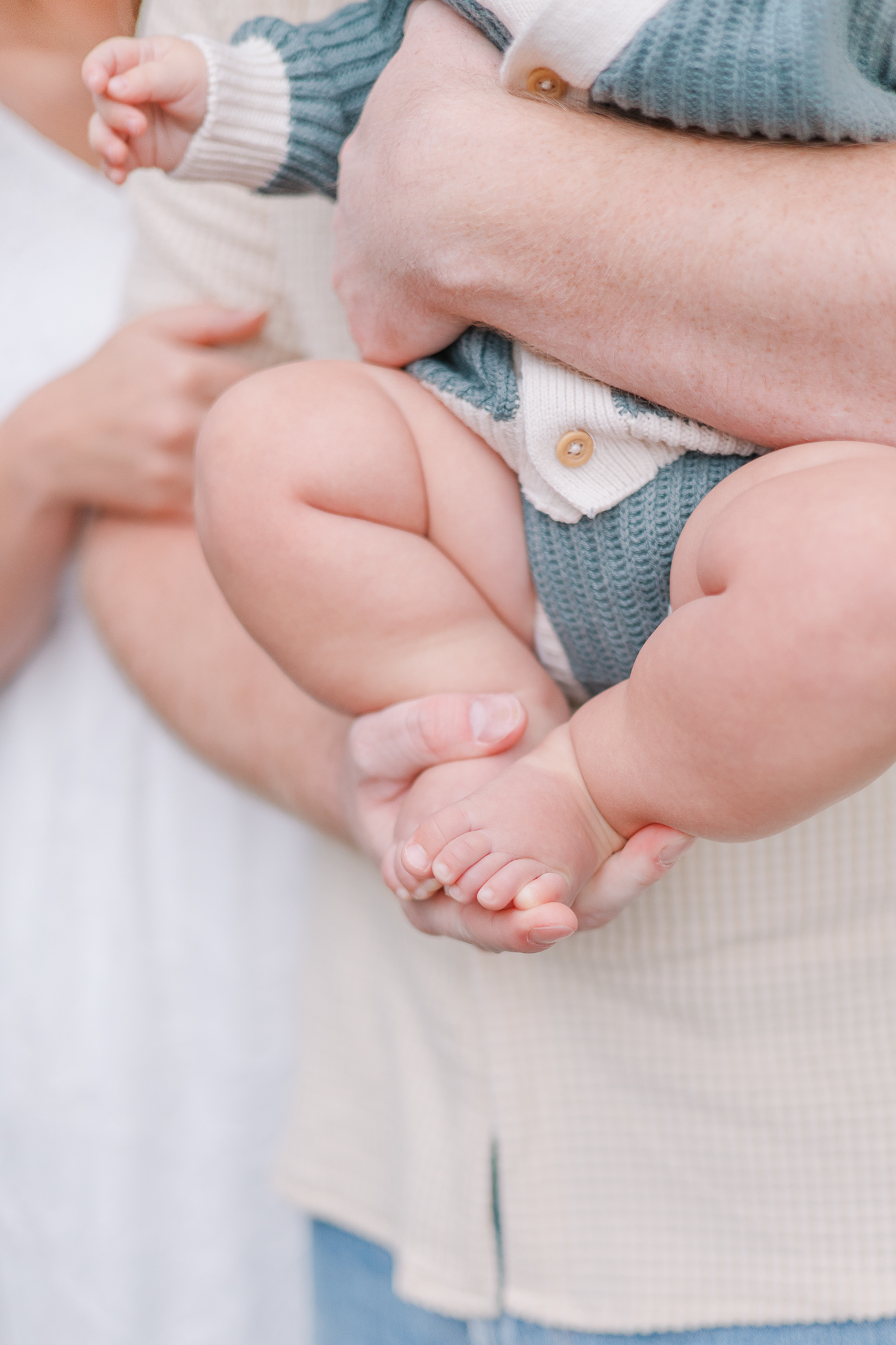 Augusta Photographer - Parents hands hold up small baby feet and legs.